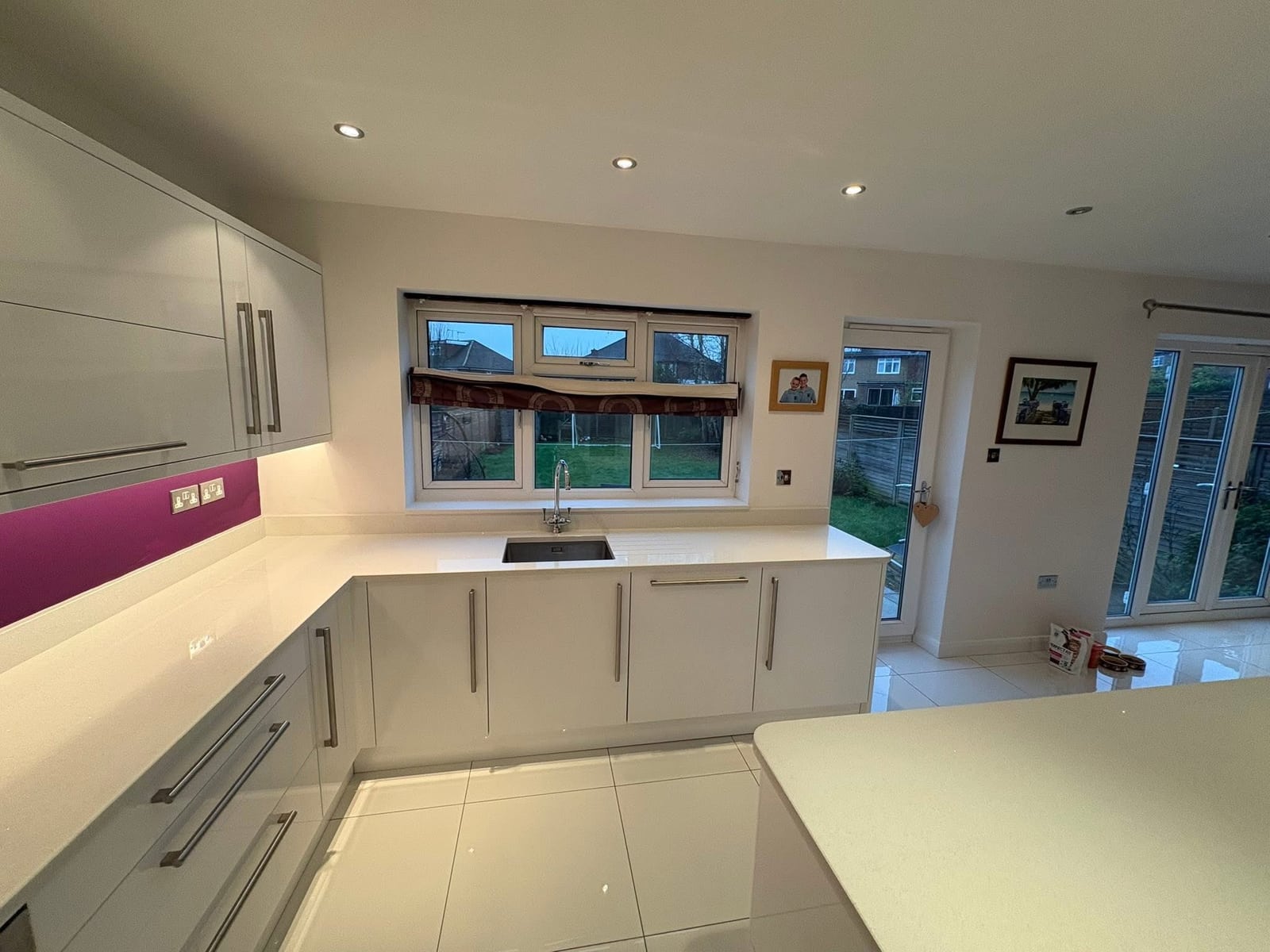 New kitchen with white gloss cabinetry, quartz worktop and sink overlooking the garden