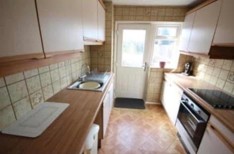 Old galley kitchen with back door at the end, showing dated tile work and cabinetry
